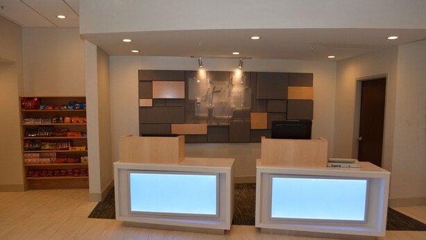 A reception area with two illuminated reception desks, a wall-mounted digital display, and a shelf with various items.