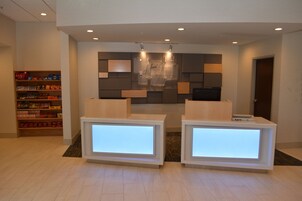 Un área de recepción con dos mostradores iluminados, una pantalla digital montada en la pared y una estantería con diversos objetos.