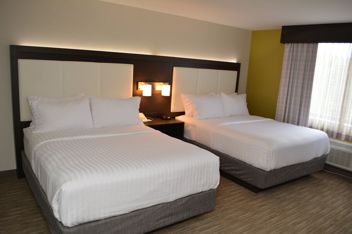 A hotel room with two beds, a nightstand, and a window with curtains.