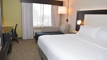 A hotel room with a large bed, a desk, a chair, a lamp, and a window with curtains.