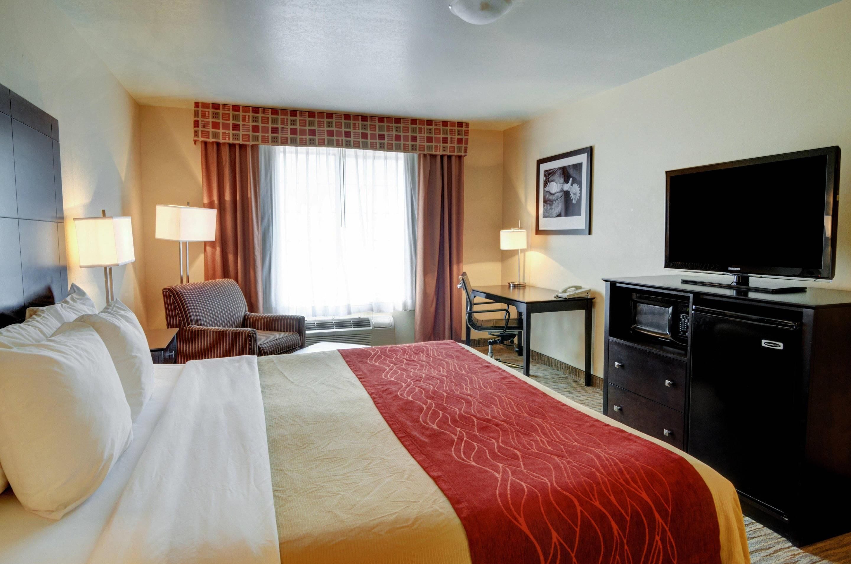 Une chambre d’hôtel comprenant un lit, deux tables de chevet, un bureau, une chaise, une télévision et un four à micro-ondes.