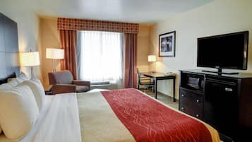 Une chambre d’hôtel comprenant un lit, deux tables de chevet, un bureau, une chaise, une télévision et un four à micro-ondes.