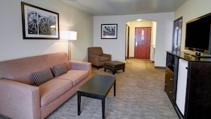 A living room with a sofa, armchair, ottoman, coffee table, TV, and artwork on the walls.