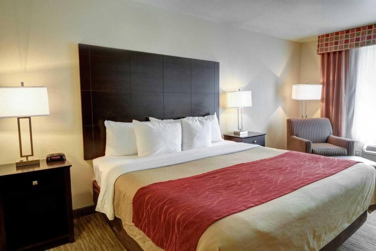 Una habitación de hotel con una cama grande, dos mesitas de noche, una silla y una ventana con cortinas.