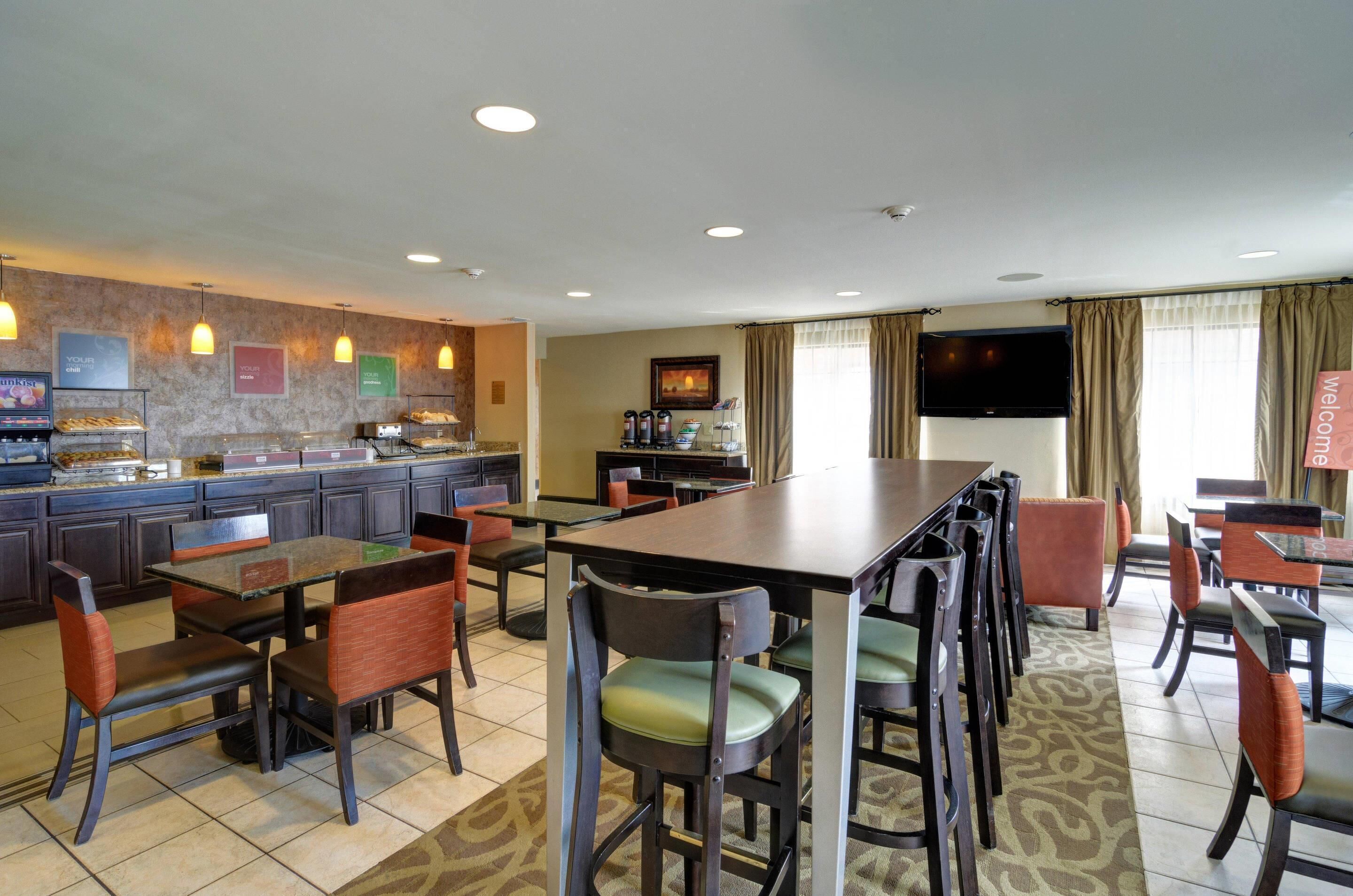A hotel dining area with multiple tables and chairs, a buffet counter, and a television mounted on the wall.