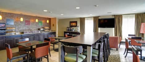 A hotel dining area with multiple tables and chairs, a buffet counter, and a television mounted on the wall.