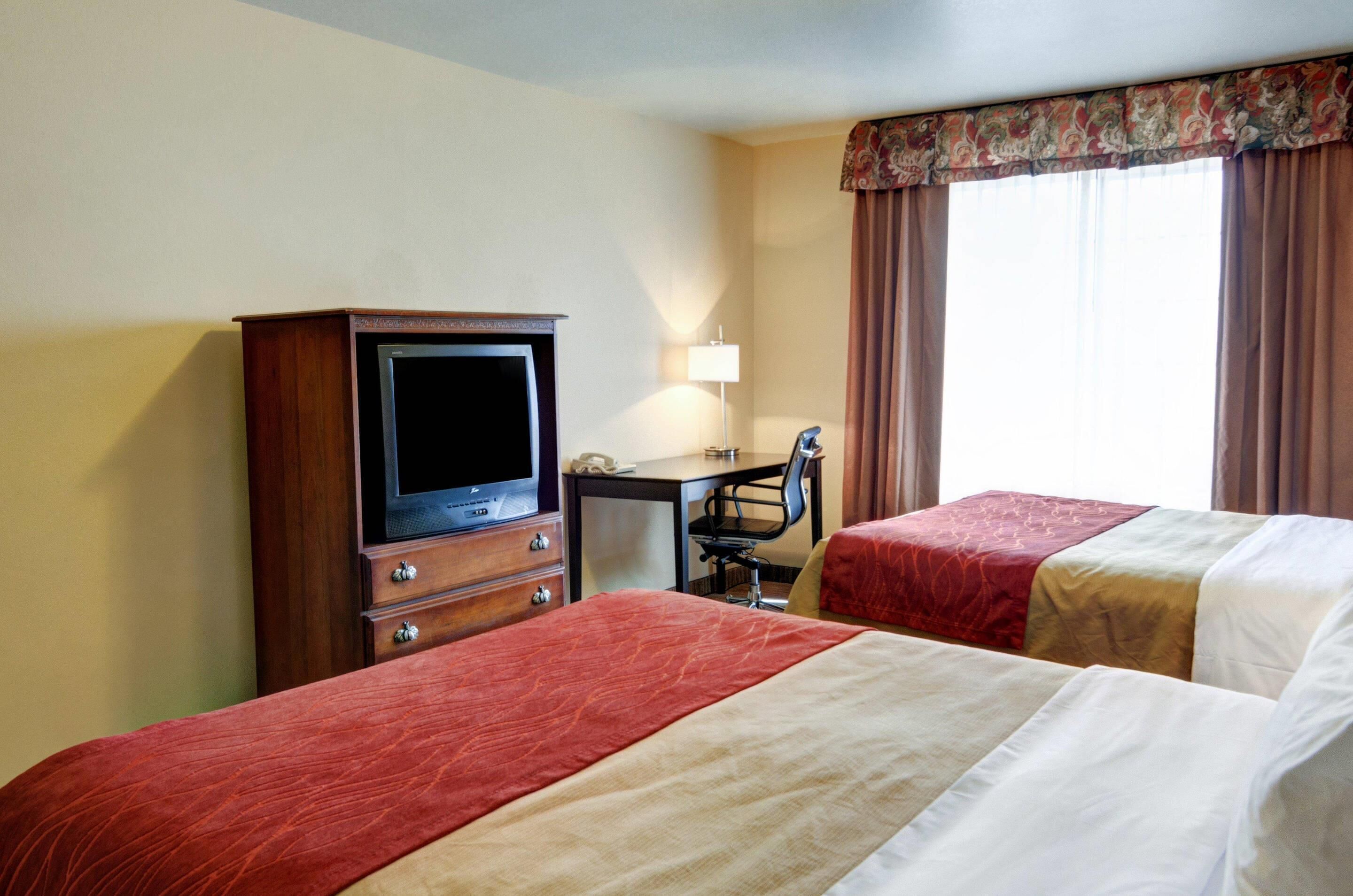 Habitación de hotel con dos camas, un escritorio con silla, televisor y lámpara.
