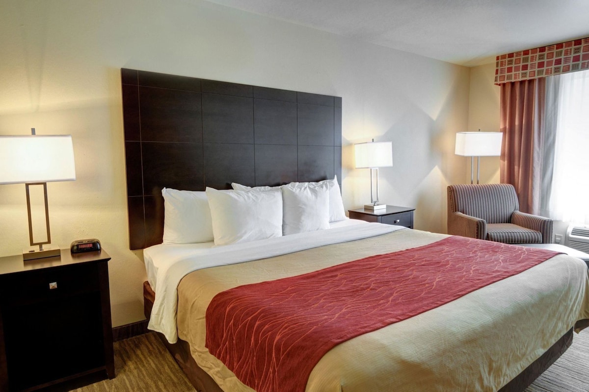 A hotel room with a large bed, two bedside tables, a chair, and a window with curtains.