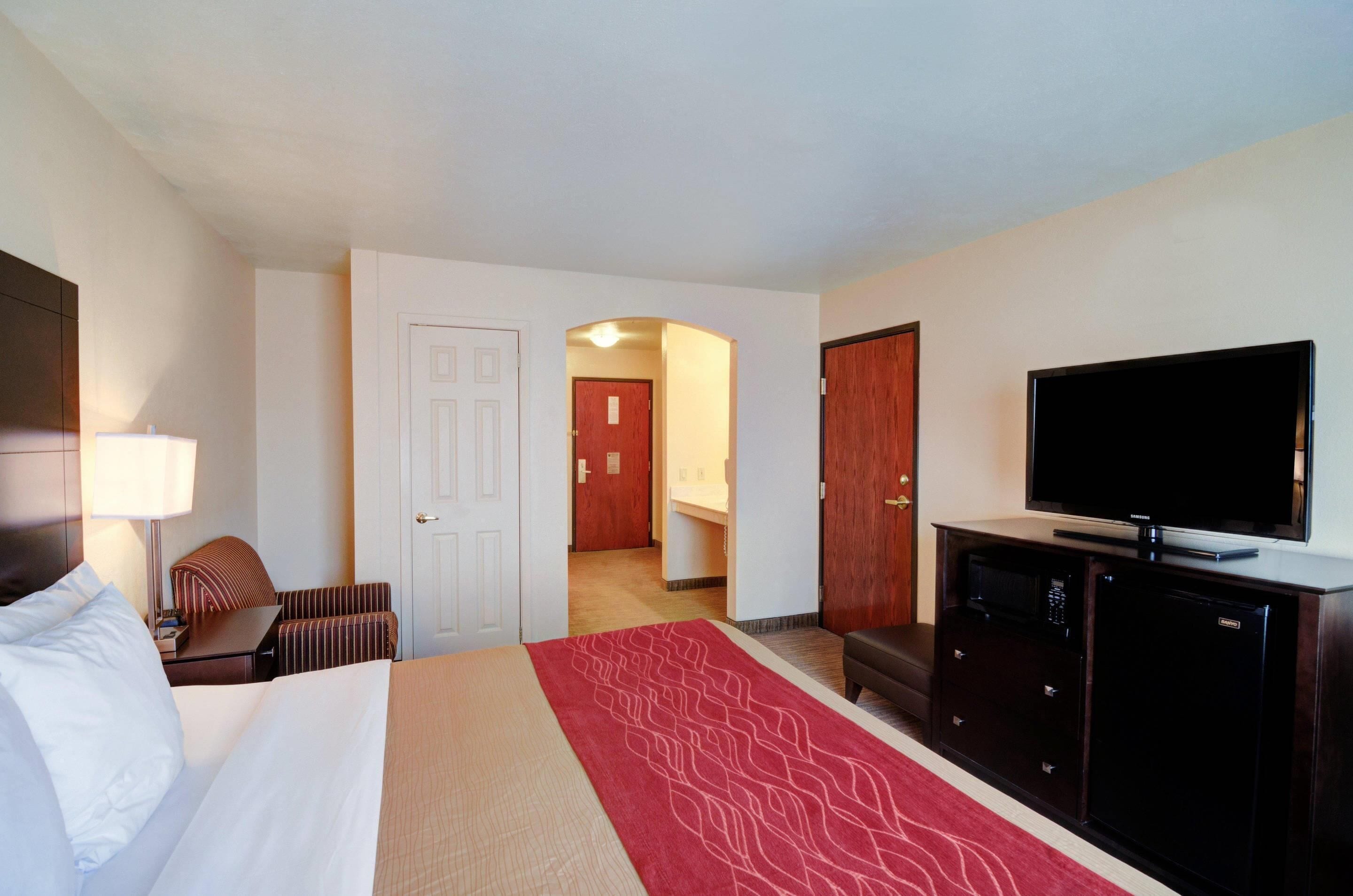 A hotel room with a bed, a television, a desk, a chair, a microwave, and a refrigerator.