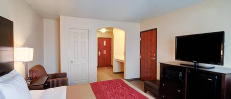 A hotel room with a bed, a television, a desk, a chair, a microwave, and a refrigerator.
