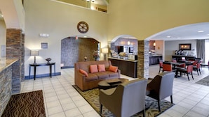 A hotel lobby with a reception desk, a sofa, a dining area, and a kitchen.