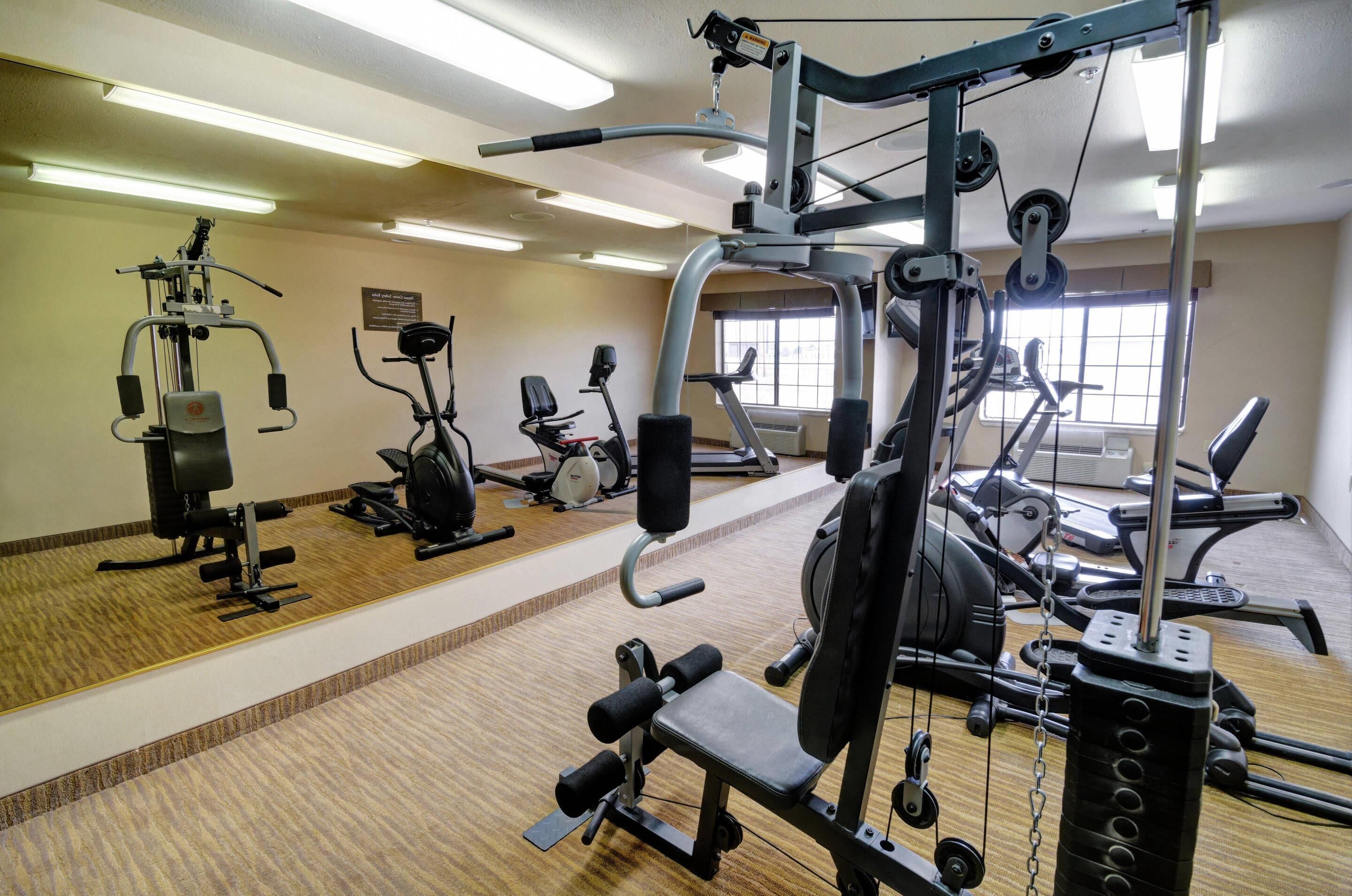 A gym with various exercise machines, a wooden floor, and a window providing natural light.