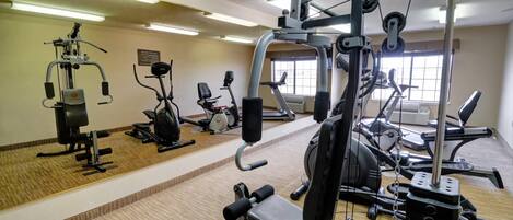 A gym with various exercise machines, a wooden floor, and a window providing natural light.