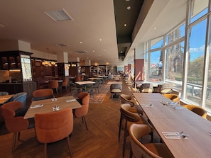 Un restaurant avec des tables et des chaises, un bar et de grandes fenêtres donnant sur un paysage agréable.