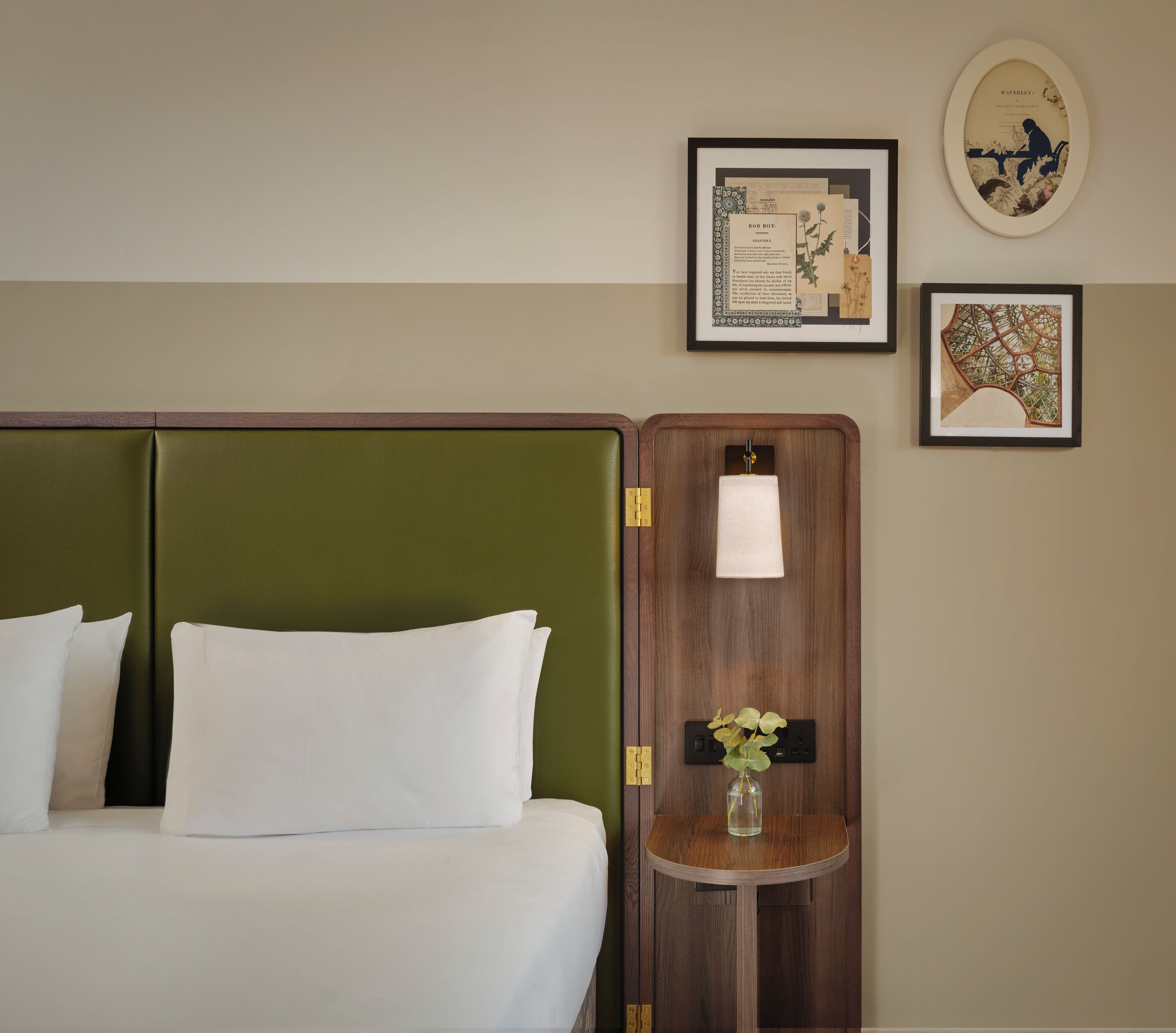A hotel room with a bed, a nightstand, and framed botanical prints on the wall.