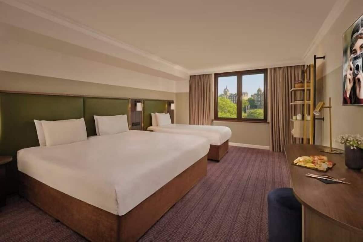 Una habitación de hotel con una cama grande, un escritorio con silla, una ventana con vistas y una lámpara.