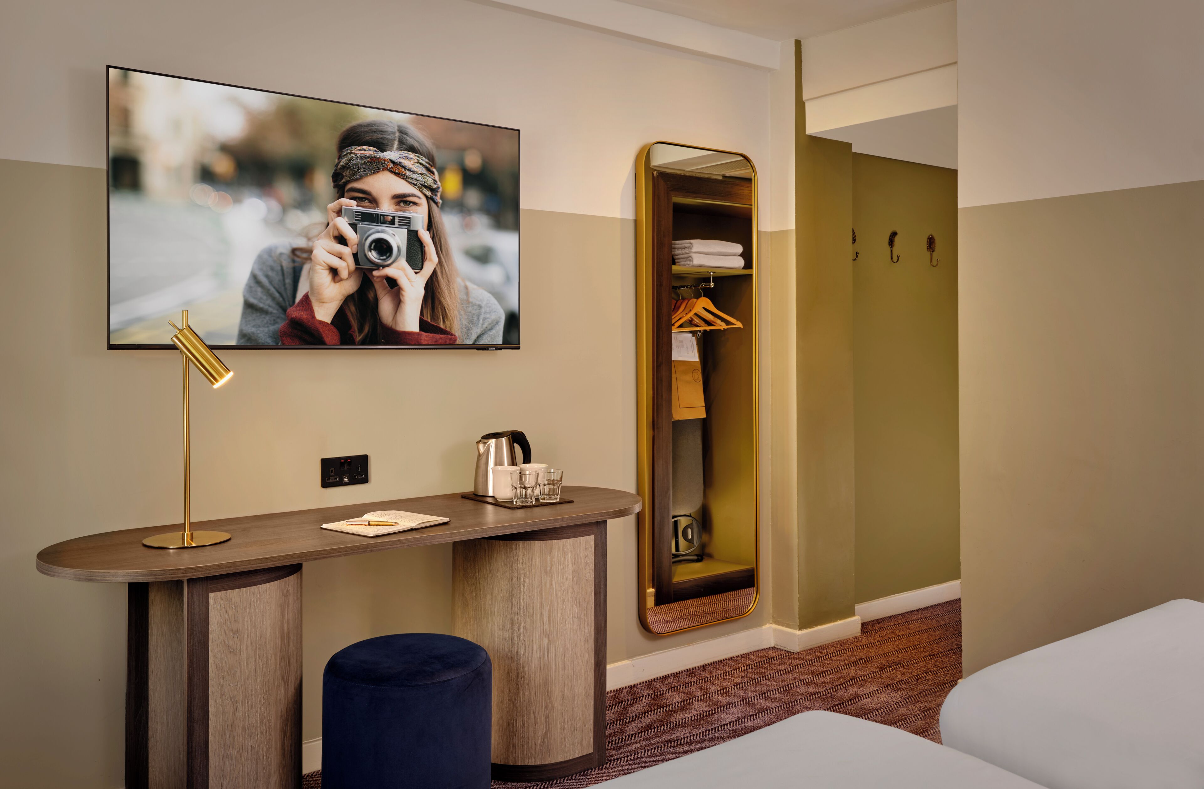 Ein Hotelzimmer mit Schreibtisch, Spiegel, Bett und Kleiderschrank.
