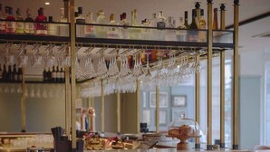 Zona de bar con taburetes, mostrador y una estantería con botellas y copas.