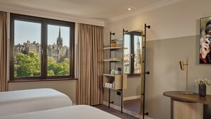 Habitación de hotel con dos camas, un ventanal con vista a la ciudad, un espejo y una mesita con un florero.