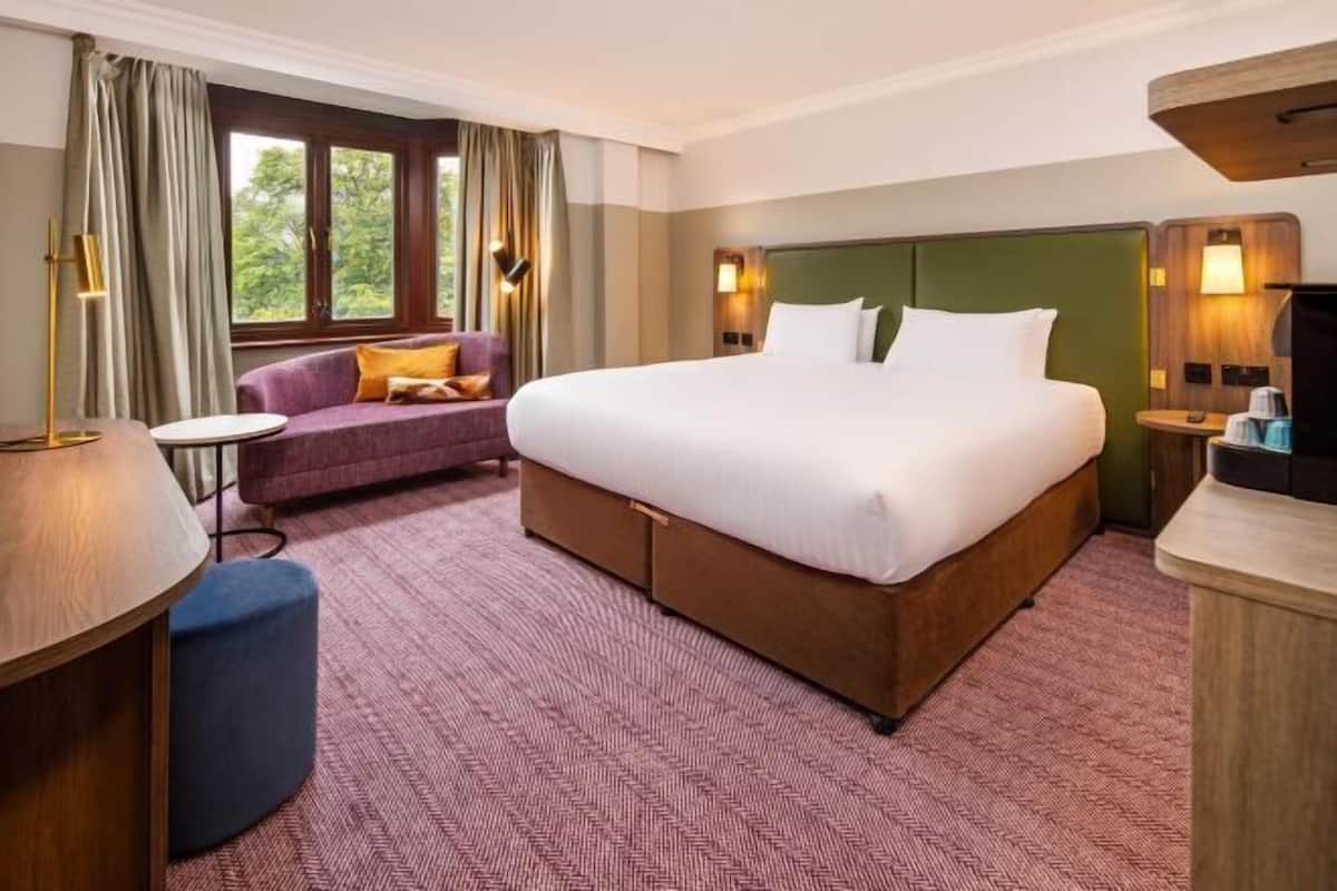 Una habitación de hotel con una cama grande, un sofá, un escritorio y una ventana con cortinas.