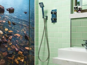 A bathroom with a glass partition, a shower with a handheld showerhead, and a sink.