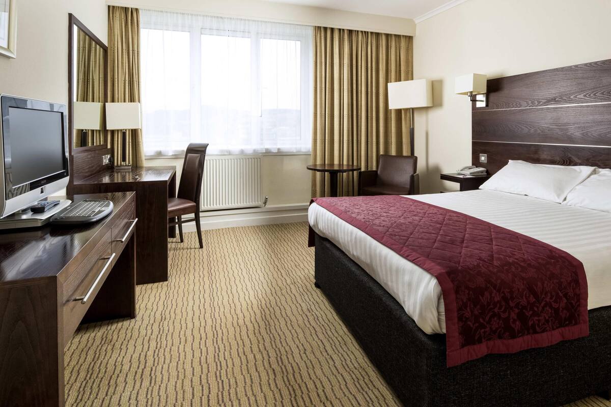 A hotel room with a bed, desk, chair, and a television.
