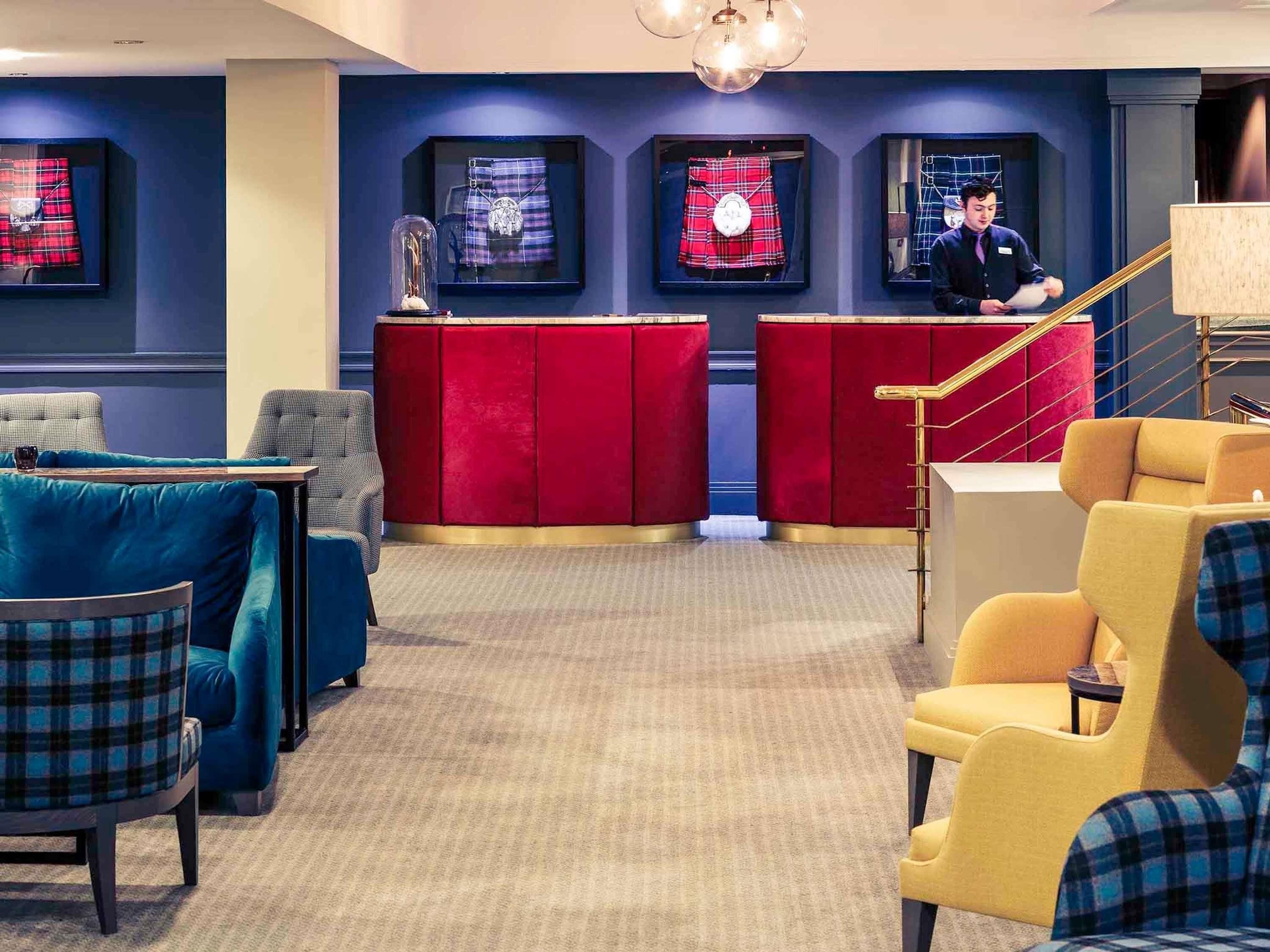 A lobby with red velvet sofas, a reception desk, and framed items on the wall.