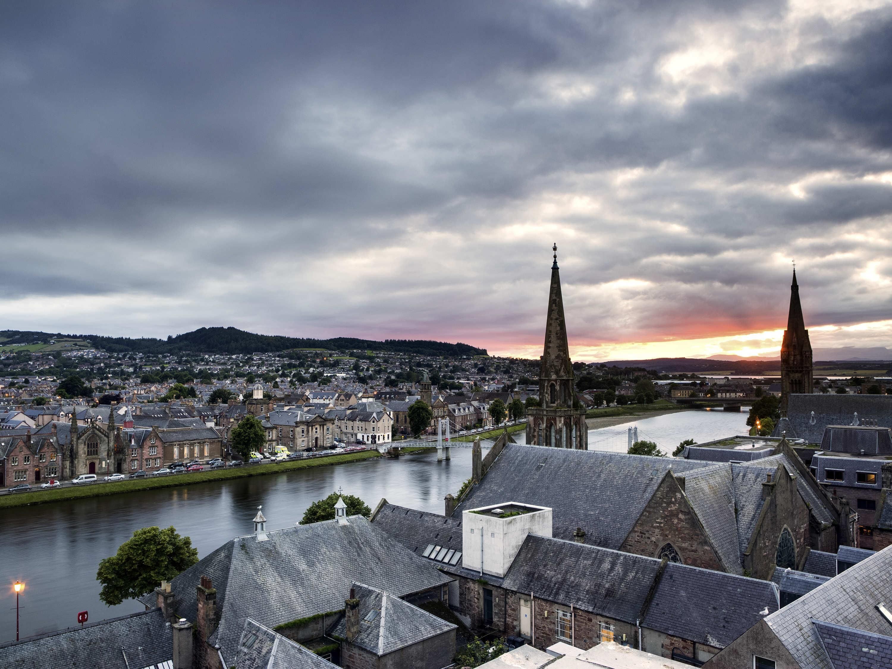 A historic town with a river, two prominent church spires, and a bridge.