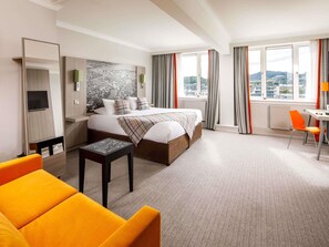 A hotel room with a bed, a desk, a chair, a TV, and a large window with curtains.