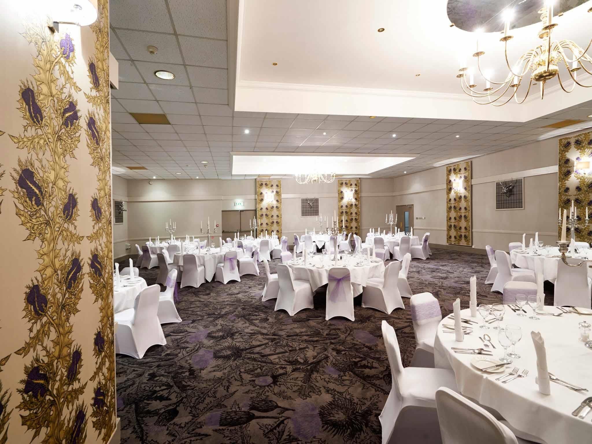 A banquet hall with round tables set for dining, white chairs, and a carpeted floor.