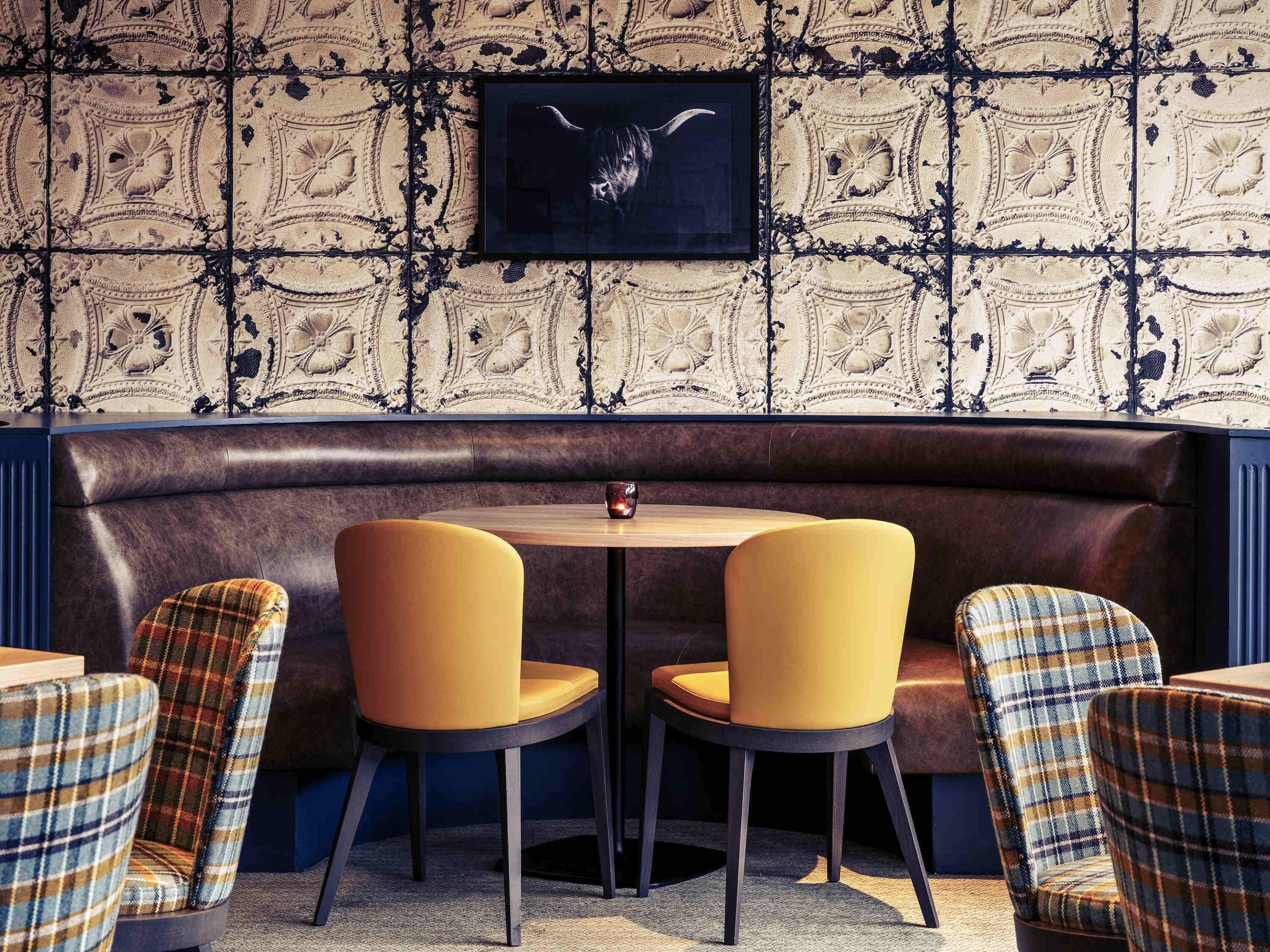 A restaurant with a dark leather booth seating area, two yellow chairs, and plaid-patterned chairs.