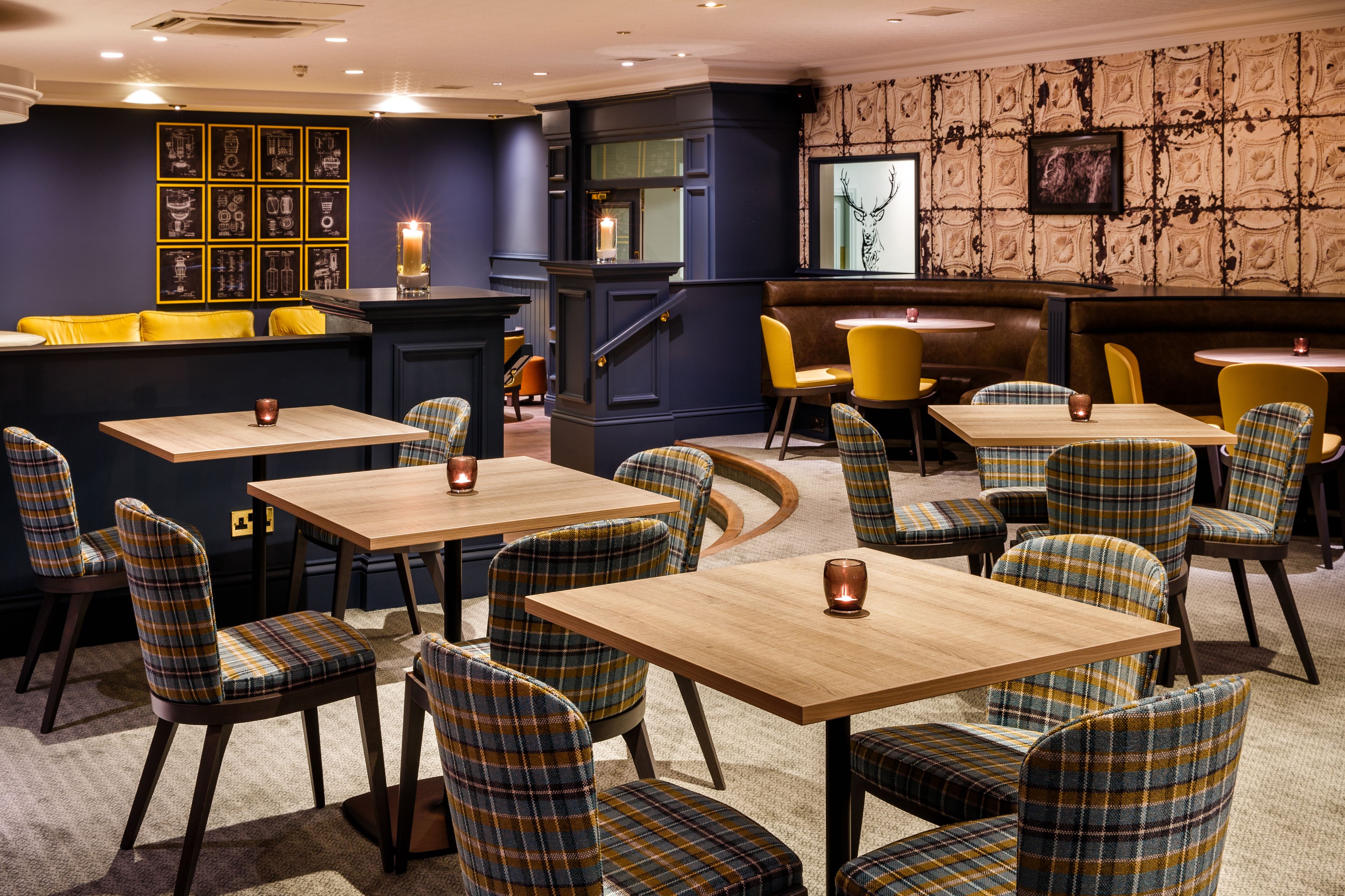 A restaurant with plaid chairs, wooden tables, and a dark blue wall with framed pictures.