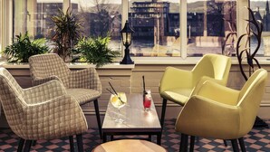 A room with a checkered floor, two armchairs, a table with drinks, and a view through large windows. - Mercure Inverness Hotel (Inverness)