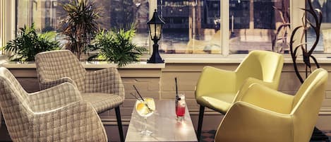 A room with a checkered floor, two armchairs, a table with drinks, and a view through large windows.