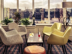 A room with a checkered floor, two armchairs, a table with drinks, and a view through large windows.