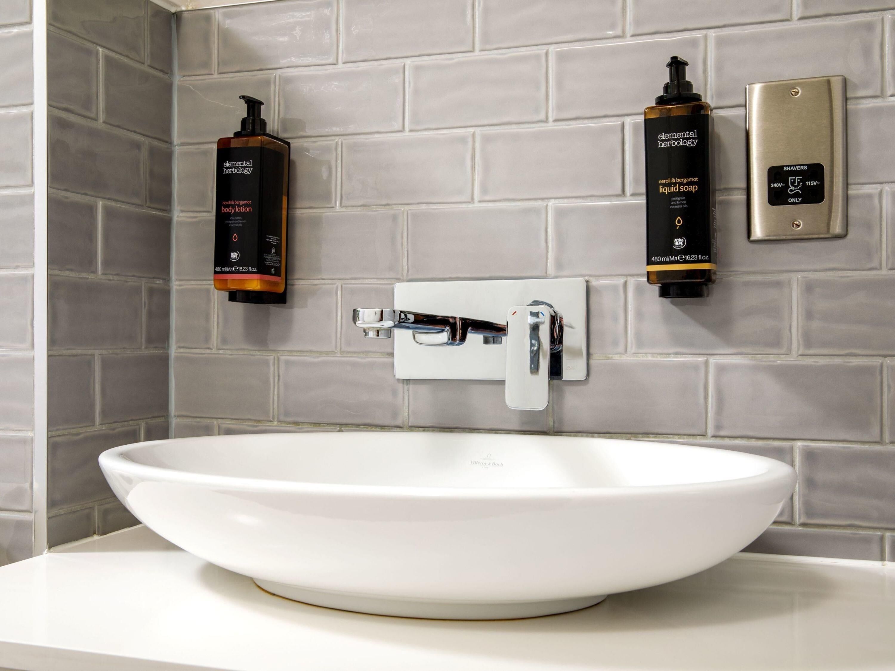 A bathroom with a white sink, a hand dryer, and two bottles of body lotion.