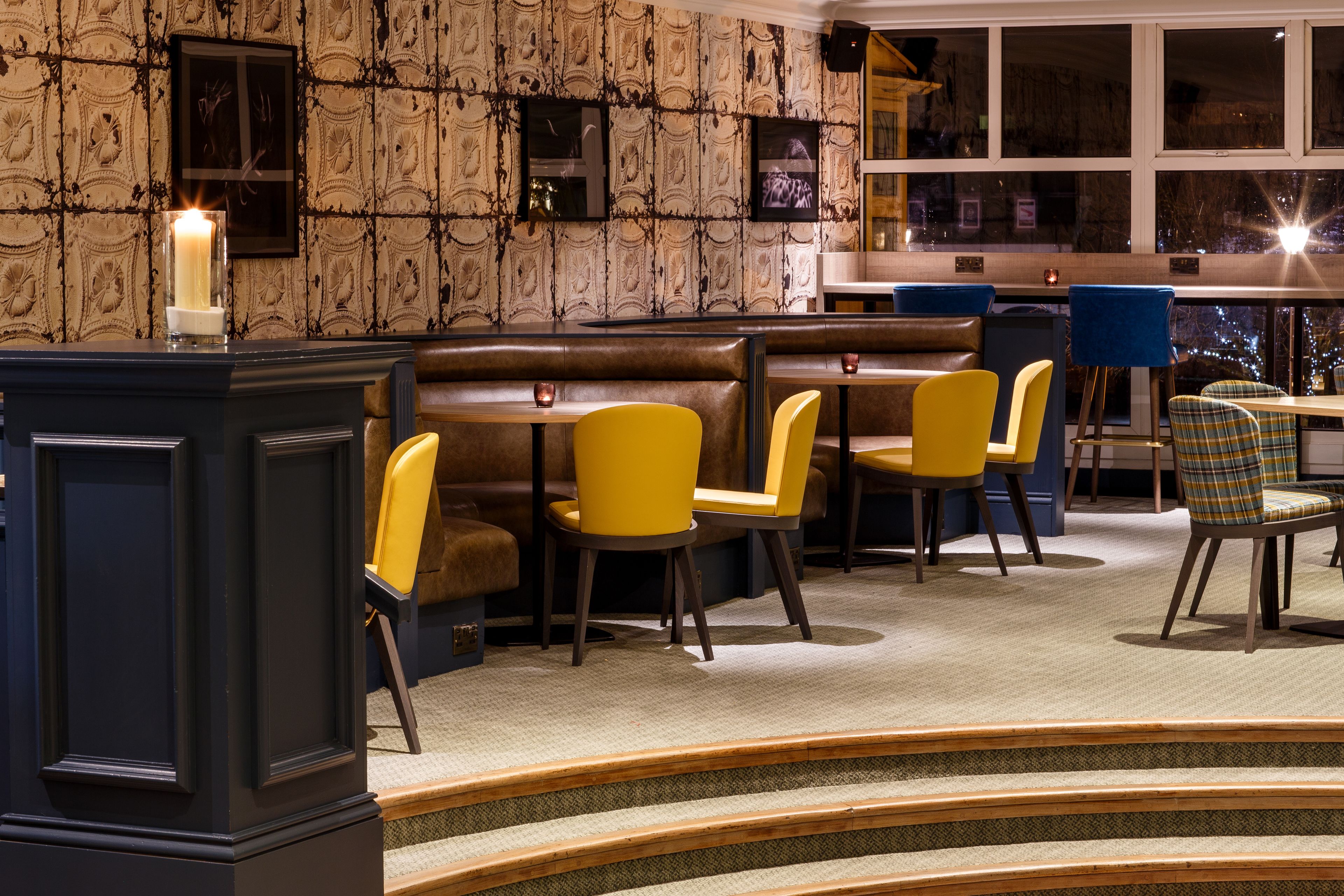 A restaurant with a patterned wallpaper, wooden benches, and yellow chairs.