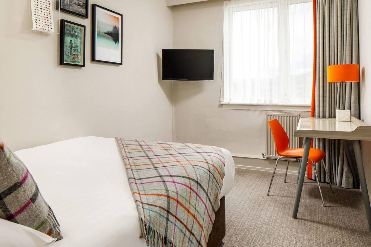A hotel room with a bed, a desk, a chair, a television, and a window with curtains.