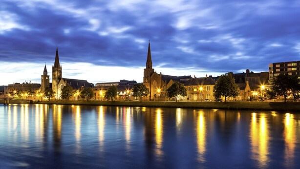 A cityscape with historic buildings and a calm river reflecting the lights.