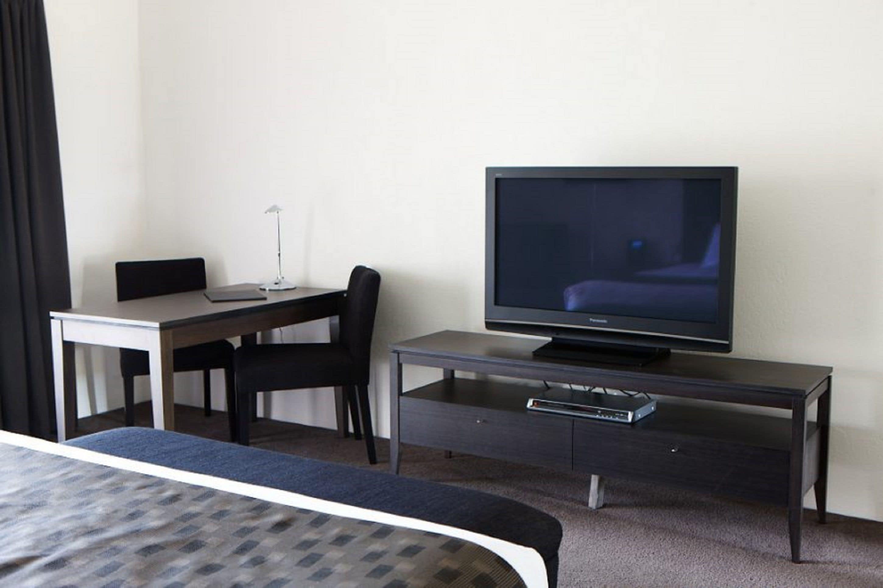 A hotel room with a bed, a desk, a chair, a television, and a small cabinet.