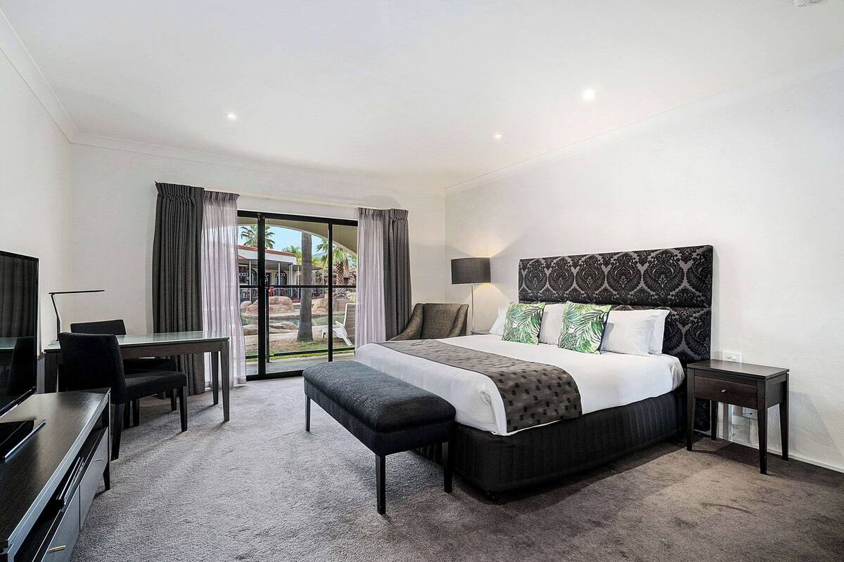 A modern hotel room with a large bed, a desk, a chair, and a TV.