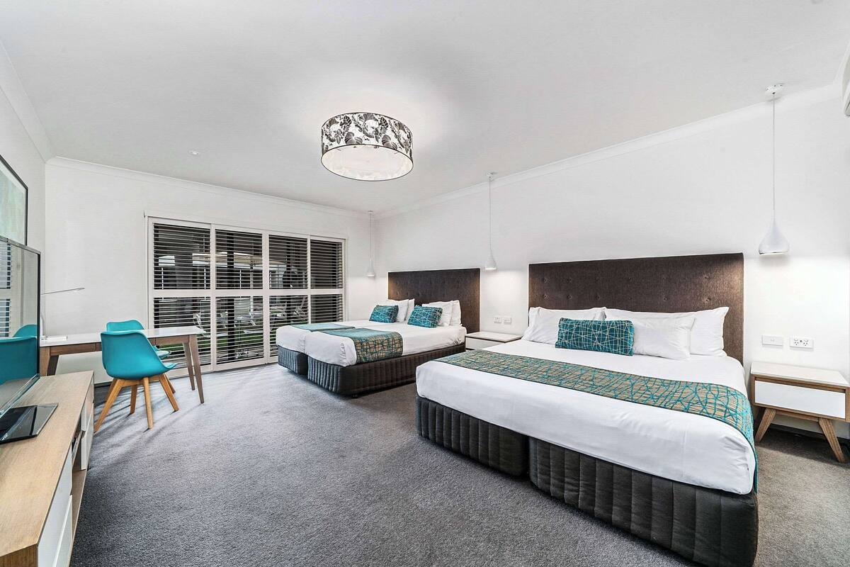 A modern hotel room with two beds, a desk, and a chair.