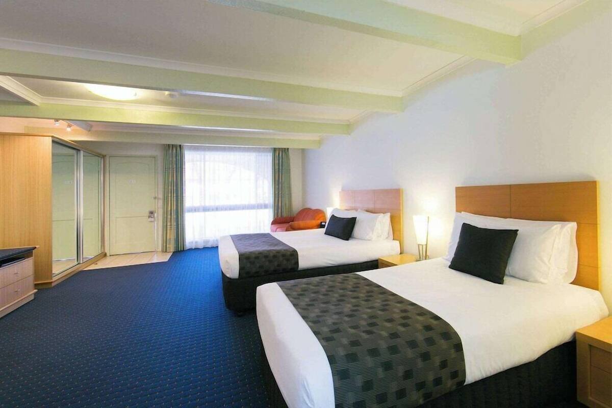 A hotel room with two beds, a desk, a wardrobe, and a window with curtains.