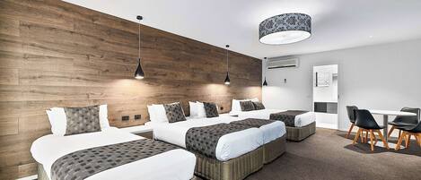 A modern hotel room with a wooden accent wall, multiple beds, a dining area, and a ceiling lamp.