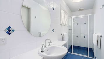 Un baño con un lavabo blanco, un espejo grande, ducha con puertas de cristal y suelo con azulejos azules.