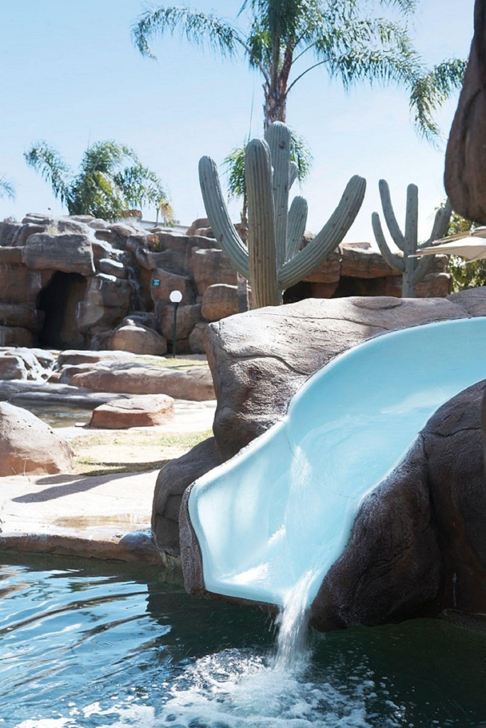 Un tobogán de agua con un paisaje rocoso y cactus al fondo.