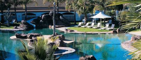 Un espace piscine aménagé dans un complexe hôtelier, offrant une vue dégagée sur la piscine, les chaises longues et les jardins environnants.