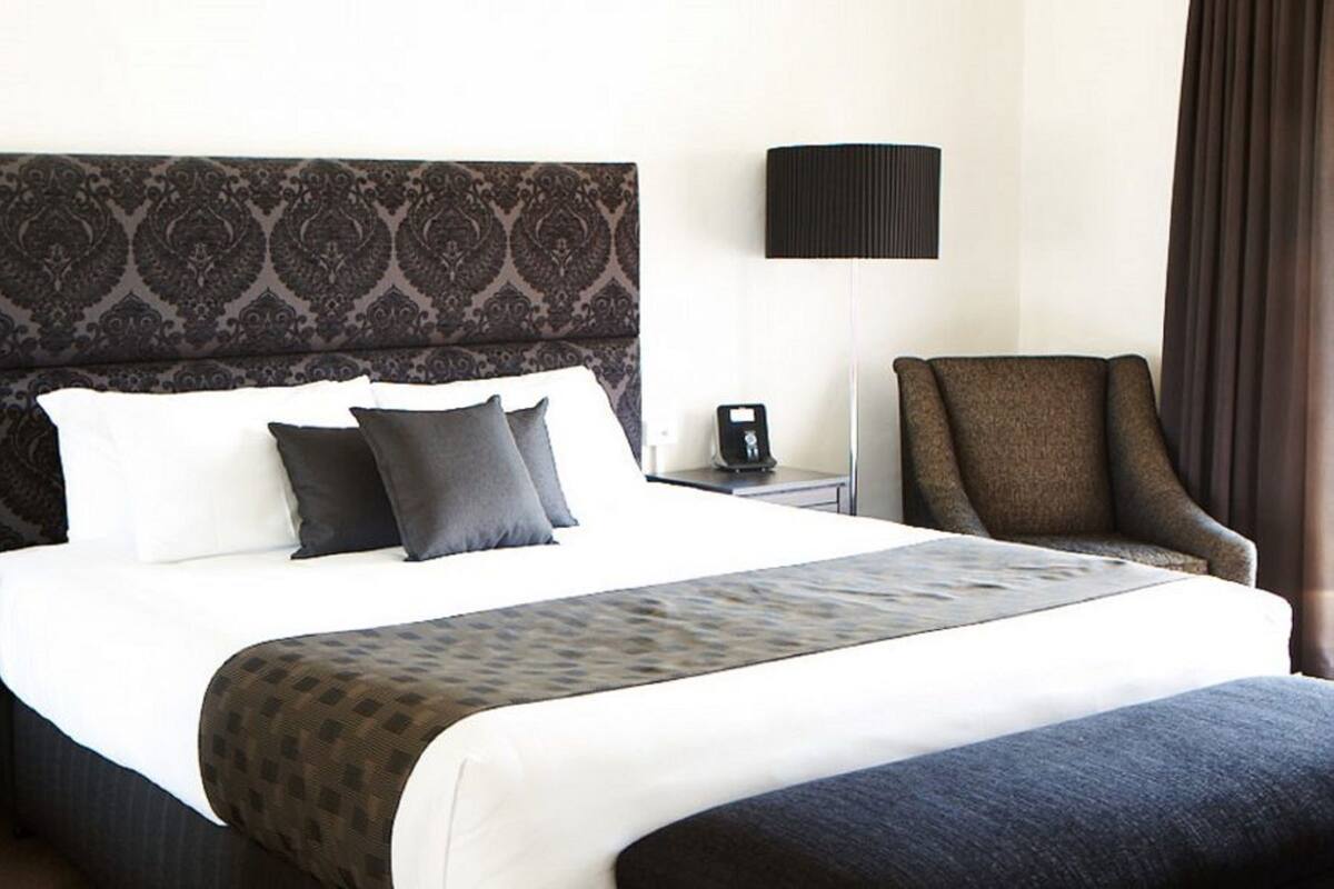 A hotel room with a large bed, a nightstand, a lamp, and a chair.