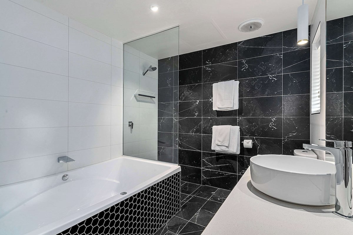 A modern bathroom with a large bathtub, a round sink, and a glass-enclosed shower area.