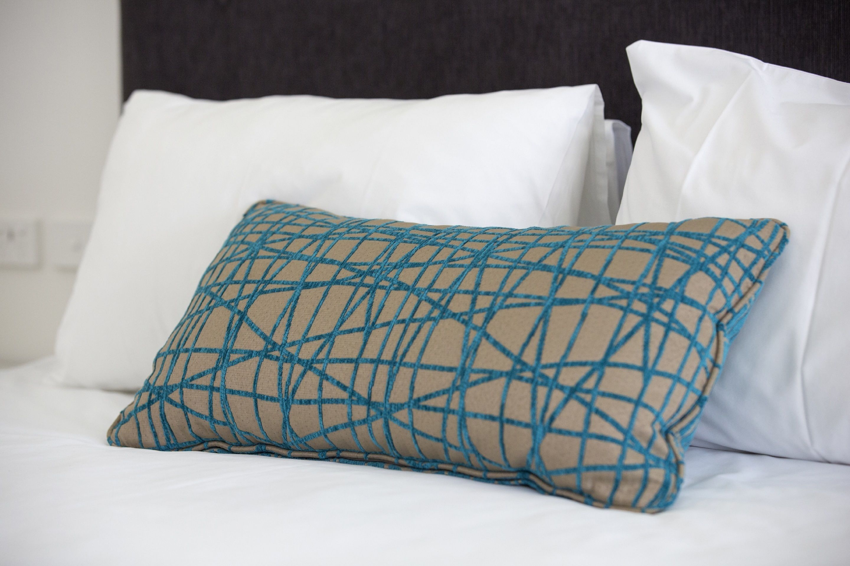 A bed with white linens and a single decorative pillow with a geometric pattern.